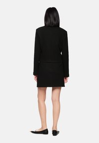 Black textured blazer dress with long sleeves, waist seam, and a straight fit. Paired with black flats featuring a pointed toe accent.
