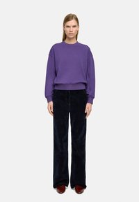 Fioletowy bawełniany sweter z prążkowanymi mankietami i dolną częścią, w połączeniu z spodniach z wysokim stanem o szerokich nogawkach z ciemnej korduroy oraz brązowymi skórzanymi butami.