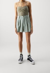 Světlé zelené zkrácené šortky se sklady, doplněné o fitted béžový top s výstřihem ve tvaru srdce a černé high-top tenisky.