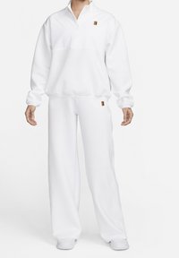 Valkoinen fleece-juoksuasu, jossa on neljännesvetoketjukaulus, pitkät hihat ja rento malli housuissa. Housuissa ja rinnassa on pieni värillinen logo.