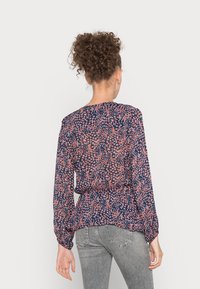 Blusa floreale blu navy con maniche lunghe, caratterizzata da un design a peplum e una vita arricciata, decorata con piccoli fiori rosa e bianchi.