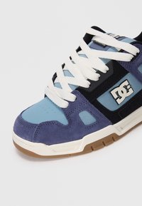 Men's sneaker with a mix of blue suede and mesh, featuring white laces, black accents, and a tan rubber sole. Logo on the side.