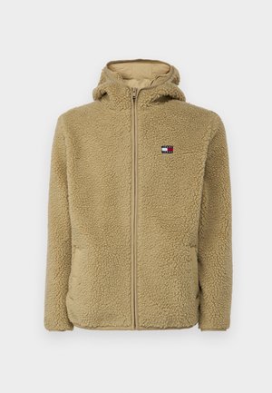 Beige fleece hoodie med fuld lynlås, struktureret stof og sidelommer. Har et lille logo på den øverste venstre brystområde.