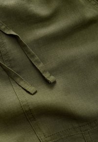 Material verde măsliniu cu o textură netedă, prevăzut cu șnururi și accente cusute, prezentând un design ușor și respirabil.