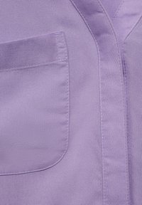 Tessuto viola con una superficie liscia, caratterizzato da una tasca cucita e dettagli di cucitura puliti, creando un design geometrico con linee angolate.