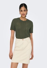 Knit green short-sleeve sweater with a textured diamond pattern, paired with a light beige denim skirt featuring a single button closure.