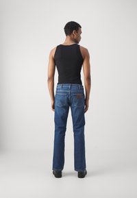 Top negru fără mâneci și blugi din denim albastru. Blugii au cinci buzunare, un design drept și o etichetă din piele maro pe talie în spate.