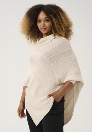 Light beige knitted poncho featuring a cowl neck, textured stripes, and a diagonal hem. Material is soft, with an oversized fit.