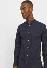 Marineblauwe button-up shirt met een staande kraag, lange mouwen en witte knopen aan de voorkant, met een gladde, gestructureerde stof.