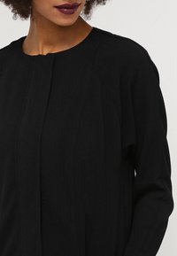 Svart långärmad topp med rundad halsringning, texturerad tyg, framvikningar och en avslappnad passform. Förstärkt med subtila sömnadsdetaljer.