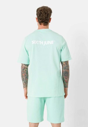 Mintgroene katoenen T-shirt en shortset, met korte mouwen, een ronde hals en een wit logo op de achterkant gedrukt.