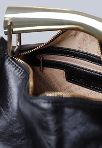 Borsa a tracolla in pelle nera con manico metallico dorato, dotata di apertura con cerniera. Interno foderato in tessuto beige e una piccola tasca con cerniera.