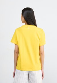 Yellow cotton t-shirt with short sleeves, featuring a round neckline and a small white logo on the back neck. Relaxed fit design.