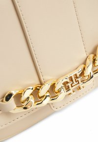 Borsa a tracolla in pelle beige con dettagli in catena dorata e logo. Texture liscia con cuciture sottili lungo i bordi.