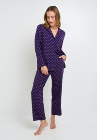 Ensemble de pyjama violet comprenant des manches longues et un pantalon, avec un motif de feuilles répétées en rose. Tissu doux et coupe décontractée.