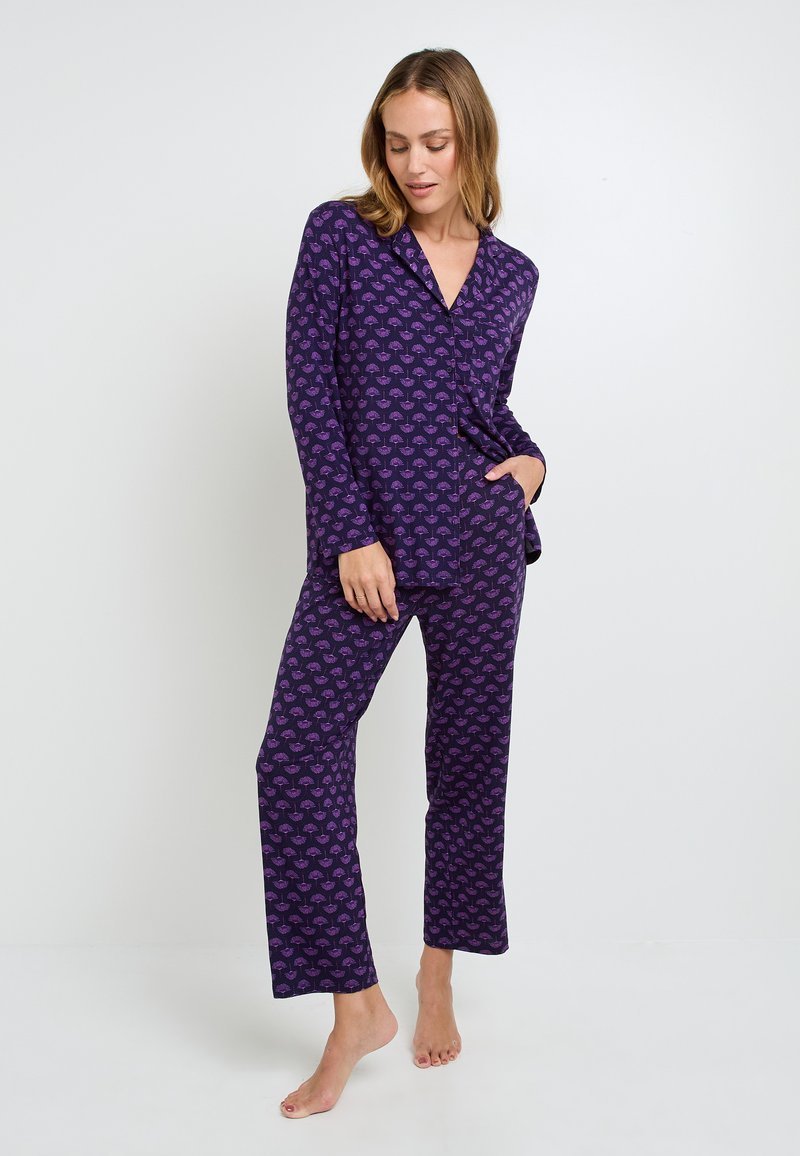 Ensemble de pyjama violet comprenant des manches longues et un pantalon, avec un motif de feuilles répétées en rose. Tissu doux et coupe décontractée.