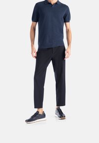 Polo shirt a maniche corte di colore blu navy, in tessuto leggero; abbinato a pantaloni neri affusolati e sneakers scure con suole bianche.