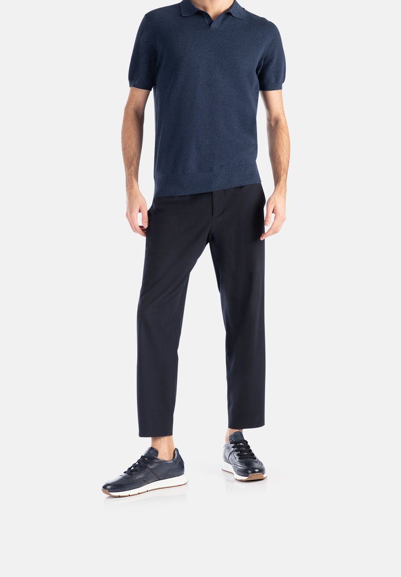 Polo shirt a maniche corte di colore blu navy, in tessuto leggero; abbinato a pantaloni neri affusolati e sneakers scure con suole bianche.