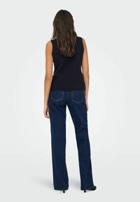 Ärmelloses, figurbetontes marineblaues Oberteil, kombiniert mit weiten, dunkelblauen Jeans. Die Jeans haben ein klassisches Fünf-Taschen-Design und sichtbare Nähte.