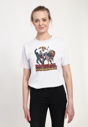 Kobieta w białej koszulce Marvel z postaciami Czarnej Pantery, Scarlet Witch, Kapitana Ameryki, Iron Mana i Thora, w połączeniu z czarnymi spodniami.