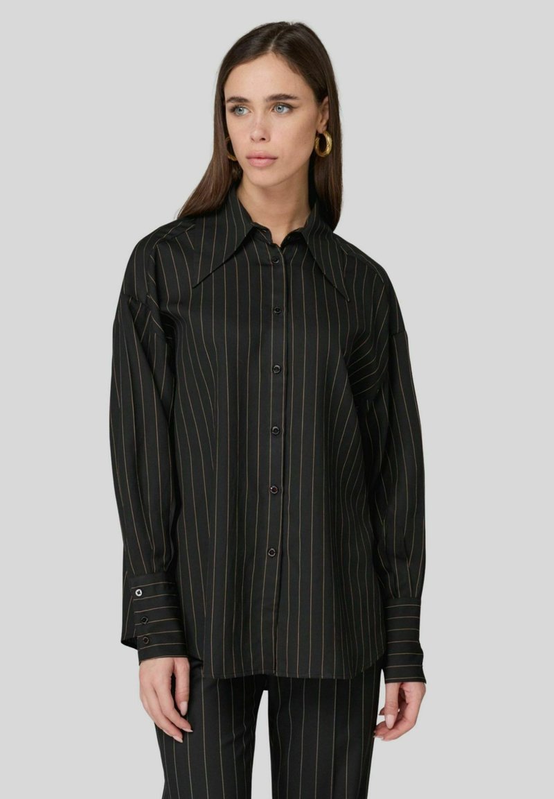 Camicia a strisce nere con colletto ampio, realizzata in tessuto liscio. Presenta chiusura con bottoni e dettagli sui polsini. Abbinata a pantaloni coordinati.