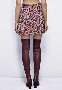 Gonna mini a fantasia floreale nei toni di viola e pesca, abbinata a stivali in pelle bordeaux alti fino alla coscia con zip e tacco inclinato.