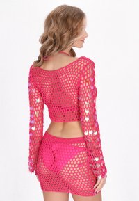 Rosa Häkel-Überwurf mit langen Ärmeln und cropped Design. Der Stoff hat ein lockeres Netzmuster mit reflektierenden Paillettenakzenten.