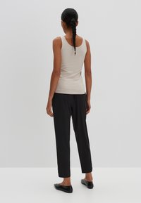 Beige fitted tank top, black tapered pants, smooth fabric, minimalistic design, slim straps. Footwear: black flats with subtle accents.