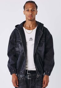 Zwarte mannen denimjas met capuchon, elastische manchetten en stervormige accenten; gedragen over een wit T-shirt met het "PXP"-logo.