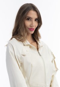 Giacca crema chiara con chiusura a zip, caratterizzata da una vestibilità rilassata, maniche oversize e dettagli delle tasche cuciti. Tessuto liscio e lucido.