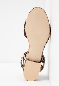 Sandale à talon imprimé léopard avec une tige texturée, dos ouvert et semelle beige. Dispose de deux lanières avec un accent bouclé pour un maintien sûr.