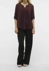 Blusa bordeaux, con texture, scollata a V e con maniche arrotolate, abbinata a pantaloni neri a gamba larga e ballerine beige.