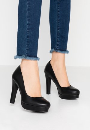 Czarne szpilki z okrągłym noskiem, gładkim skórzanym wykończeniem i platformą z przodu. Połączone z niebieskimi dżinsami z postrzępionymi mankietami.