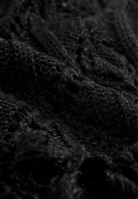 Tissu en tricot noir avec un motif texturé et en relief. Le matériau semble doux avec un léger éclat, créant une surface détaillée et accueillante.