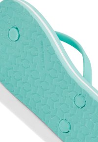 Turkoosi varvastossun pohja, jossa on teksturoitu kuvio, kaksi pyöreää reikää ja valkoiset korostusraidoitukset. Valmistettu kumin materiaalista, kestävä muotoilu.
