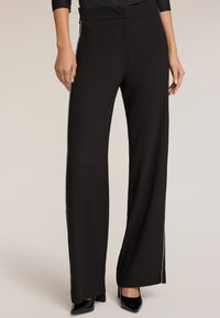 Zwarte wijde broek met een gladde textuur, voorzien van glanzende zijkanten en een op maat gemaakte taille. Gecombineerd met zwarte hoge hakken.