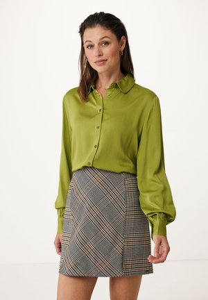 Blusa di raso verde con colletto e bottoni abbinata a una minigonna scozzese nei toni del nero, bianco e arancione. Tessuto testurizzato e design aderente.