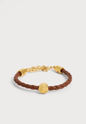 Pulsera trenzada de cuero marrón con cierres dorados, una cadena dorada y un emblema redondo de oro en el centro sobre un fondo blanco liso.
