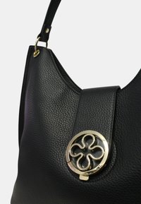 Sac à main en cuir noir avec une finition texturée, doté d'un accent en métal circulaire doré avec un motif floral à l'avant. Bandoulière ajustable.