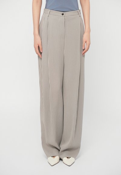 Ribede brede bukser i beige og grå med høj talje, frontfolder og sidelommer. Stylet med spidse hvide sko.
