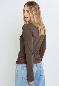 Maglia a maniche lunghe marrone in texture a coste, dal design aderente, con scollatura rotonda. Abbinata a jeans in denim blu chiaro, con attenzione ai dettagli del colletto e delle maniche.