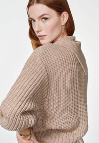 Jasnobeżowy sweter dzianinowy o prążkowanej strukturze, z kołnierzem szalowym i opuszczonymi ramionami. Elastyczne mankiety i dół.