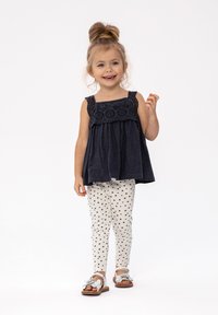 Marineblå ærmeløs top med blonderdetaljer, parret med cremede leggings med sorte hjerte-mønstre. Sølvfarvede sandaler med blomsterdetaljer.