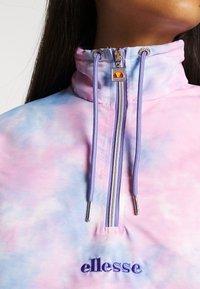 Kolorowa kurtka z ćwierć zamkiem w stylu tie-dye w pastelowych odcieniach różu i niebieskiego. Posiada srebrny zamek, fioletowe sznurki oraz haftowane logo "ellesse".