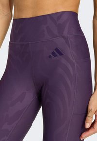 Lila Sportleggings mit strukturiertem Zebramuster, hohem Bund und einem Adidas-Logo auf der Seitentasche.