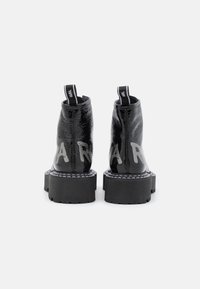 Black patent leather ankle boots feature thick platform soles, white stitching, and embossed letters on the back. Two pull tabs for easy wear.
