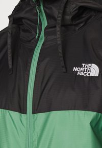 Veste The North Face noire et verte avec capuche, fermeture éclair verte et logo blanc sur la partie supérieure droite de la poitrine.