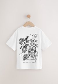 Camiseta blanca de algodón con un dibujo en línea negra de un jarrón con flores, una cesta de pan y la frase "BON APPÉTIT AMOUR".