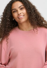 Felpa rosa chiaro con scollatura rotonda e vestibilità comoda. Tessuto morbido con leggera elasticità, caratterizzata da maniche raglan e cuciture a vista.