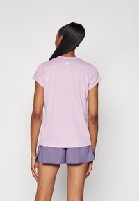Kurze Ärmel, eng anliegendes Sportshirt in helllila, aus feuchtigkeitsableitendem Material. Mit kleinem Logo am Kragen. Kombiniert mit lila Shorts.